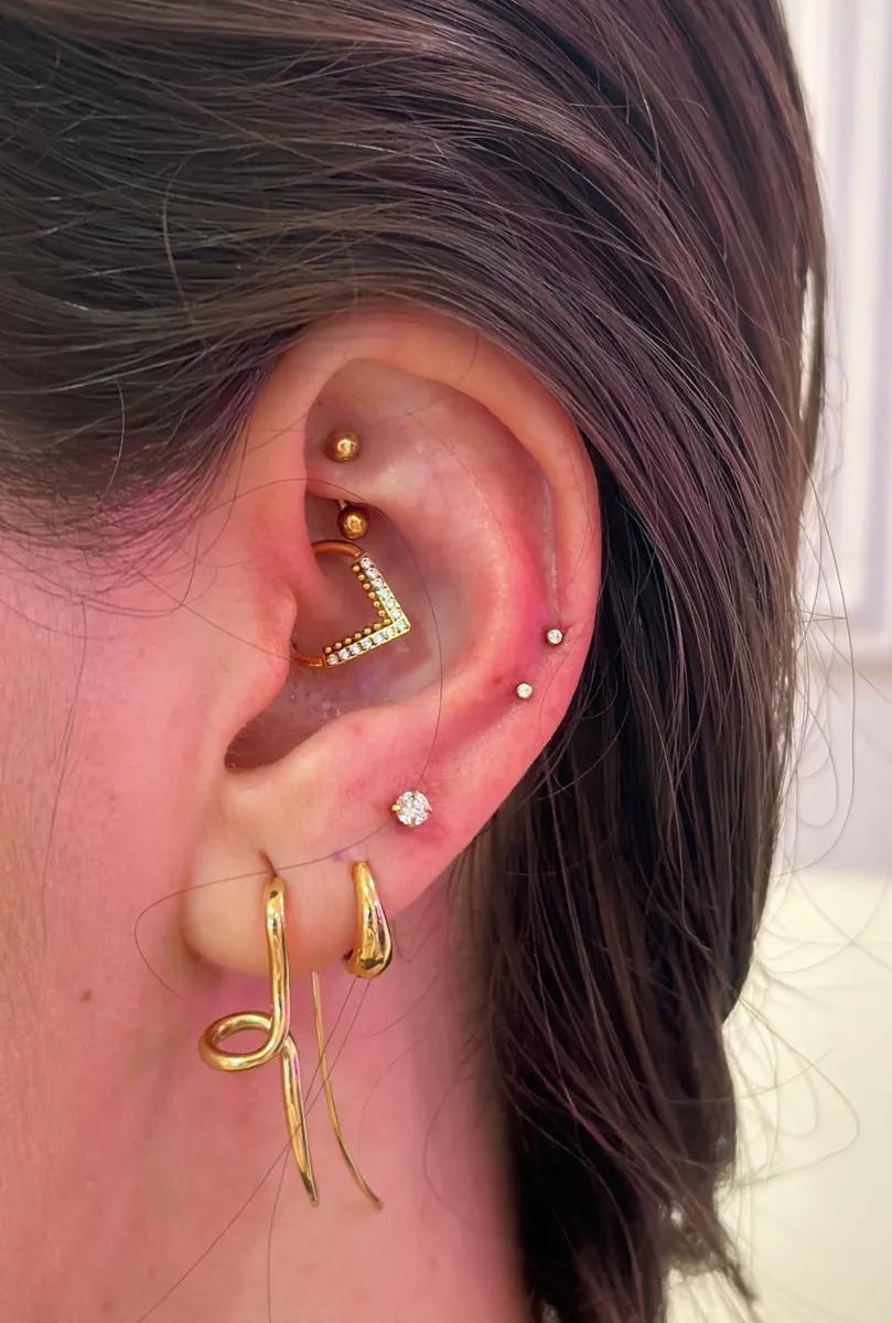 Projeto de piercings humanizados na orelha — Luquini Estética Auricular RJ Projeto de piercings na orelha com joias de ouro: daith em V cravejado, helix, trágus e brincos no lóbulo — composição da Luquini Estética Auricular no Rio de Janeiro