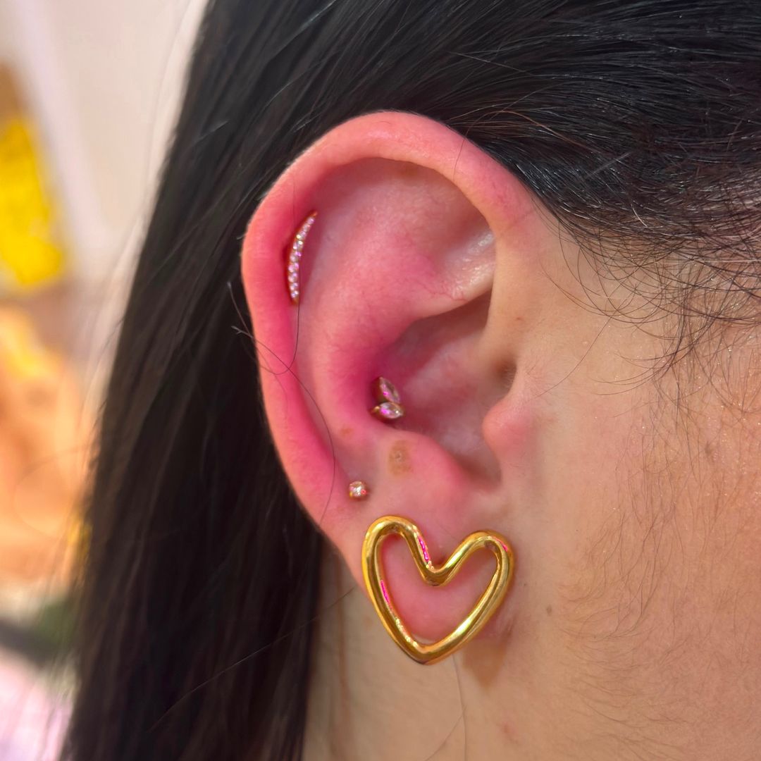 Composição auricular com brinco de coração vazado e piercings helix — Luquini Clinic, Rio de Janeiro