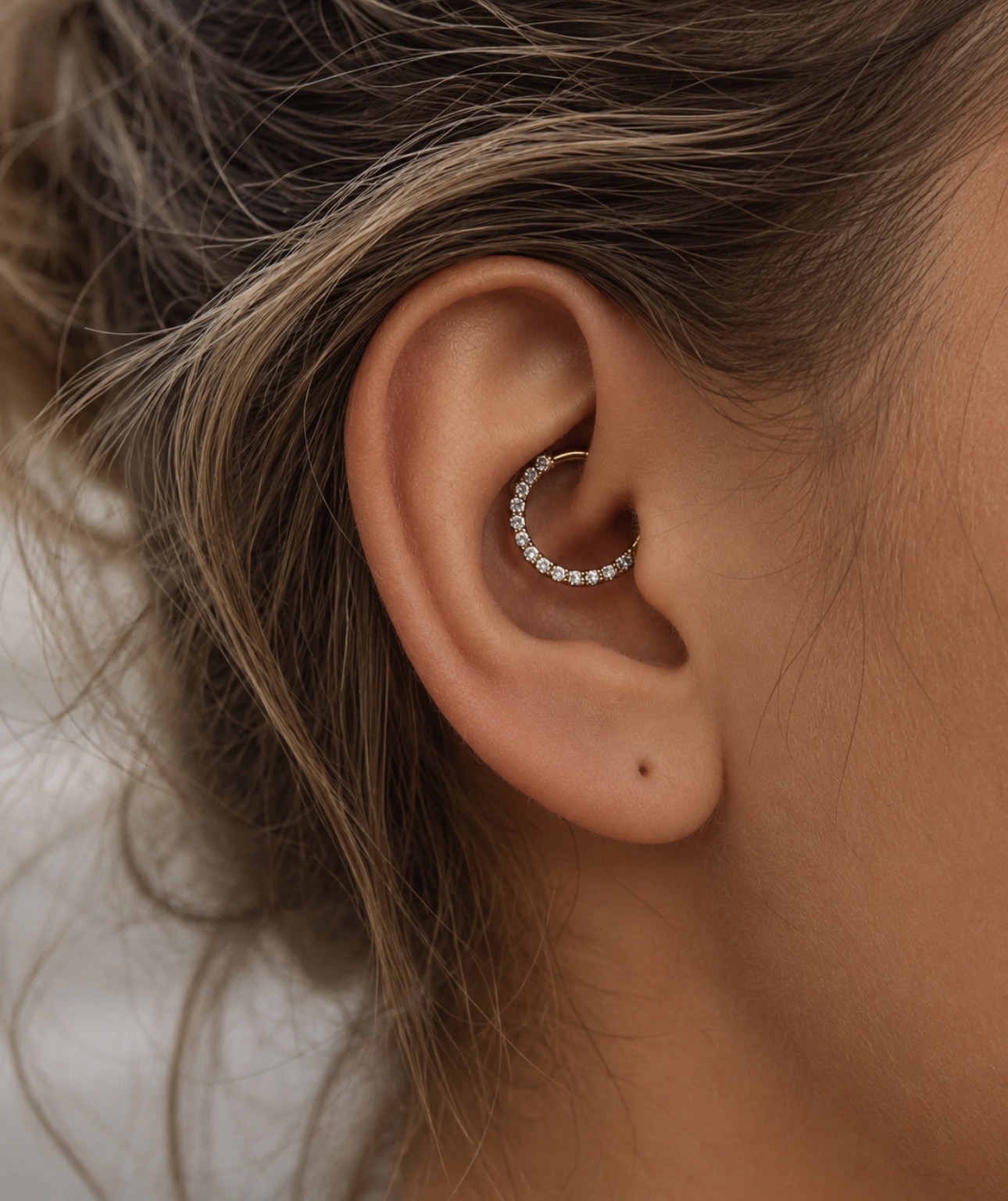 Piercing daith com argola dourada cravejada na dobra interna da cartilagem da orelha — Luquini Estética Auricular