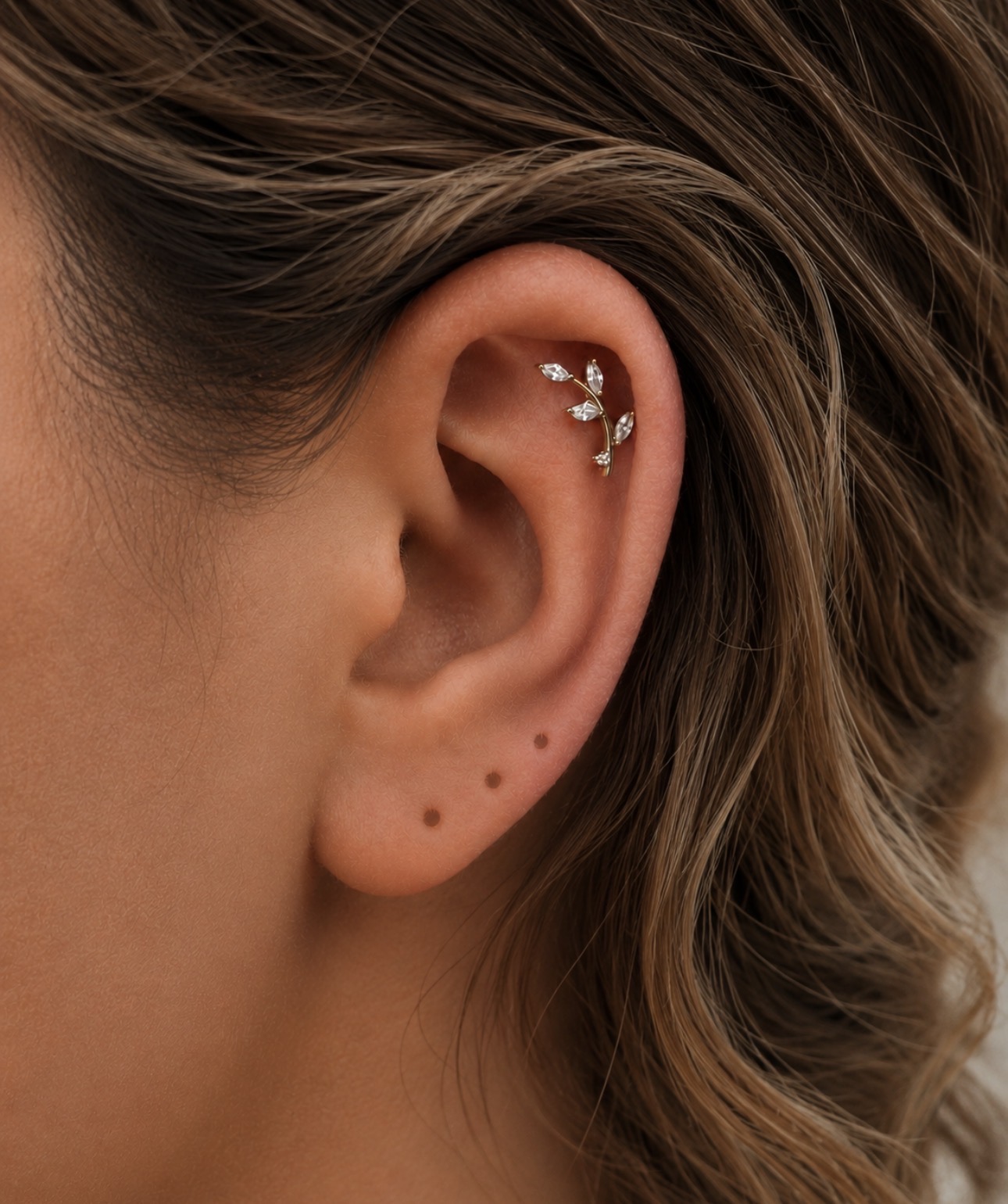 Piercing helix na cartilagem superior da orelha com joia dourada em formato de folhas — Luquini Estética Auricular