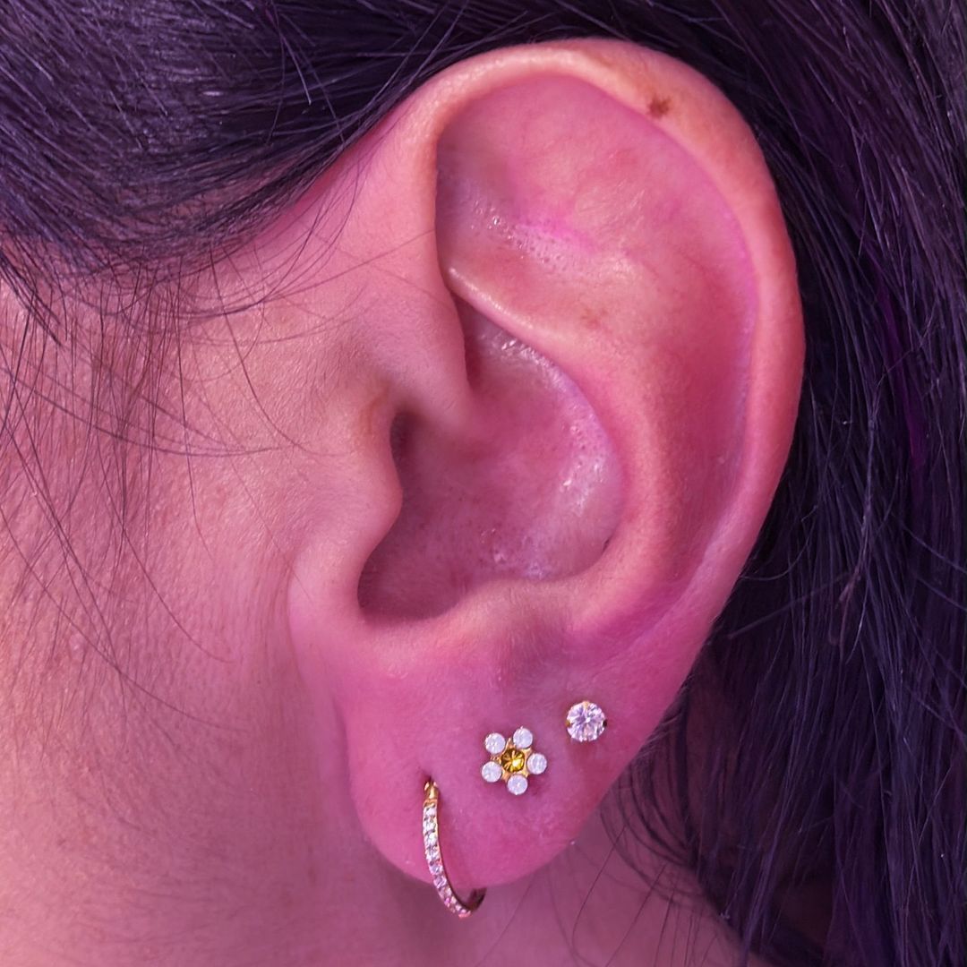 Composição auricular no lóbulo com brinco de flor e argola cravejada em ouro — Luquini Clinic, Rio de Janeiro